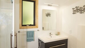 A bathroom with a white sink, dark cabinet, and a wooden-framed mirror. - Treescapes (Punakaiki)