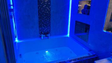 A modern bathroom with a large bathtub, a shower area, and a small window with towels.