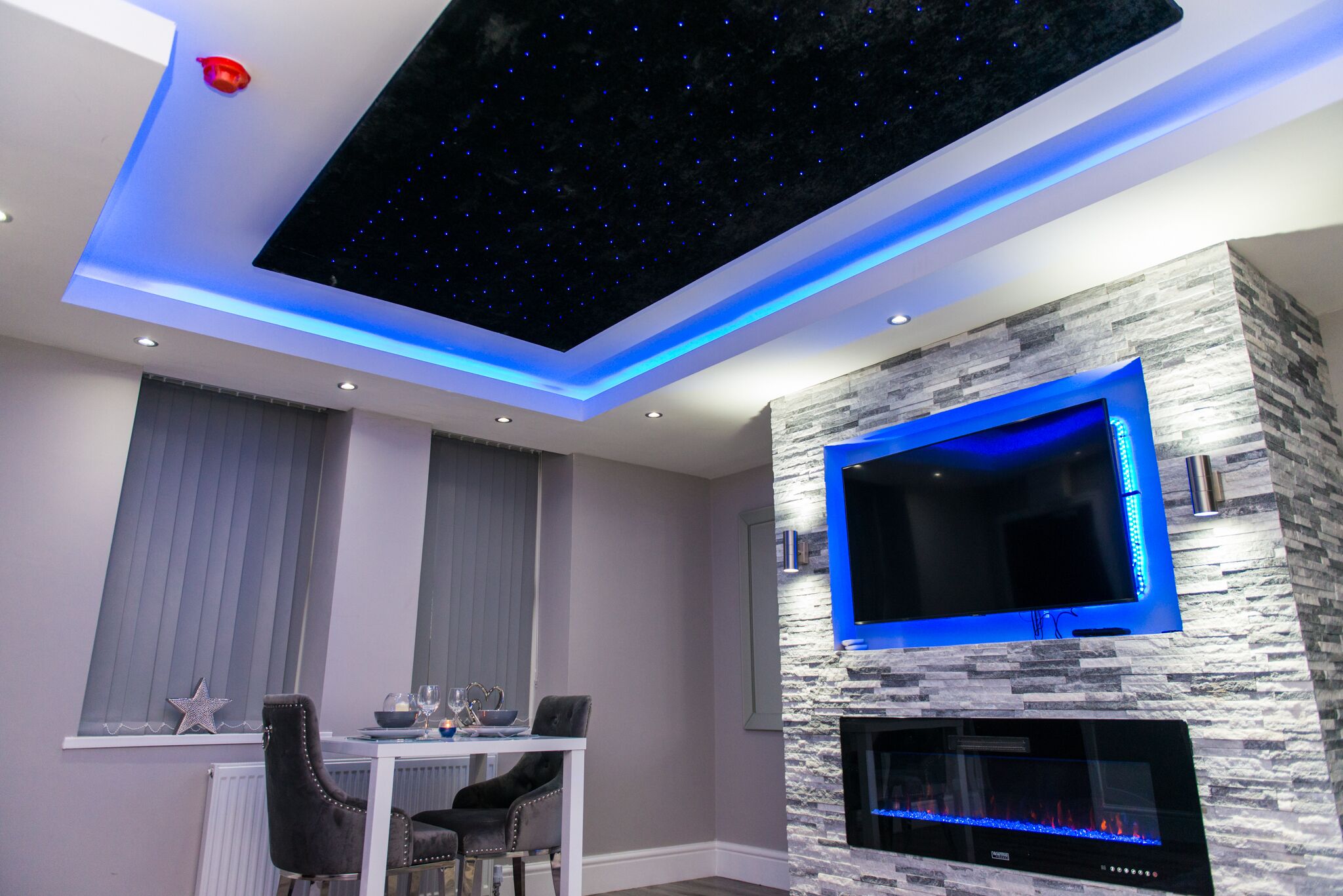 Een moderne woonkamer met een gashaard in een stenen muur, een flatscreen televisie en een plafond met een sterrenlicht ontwerp.