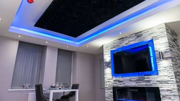 Een moderne woonkamer met een gashaard in een stenen muur, een flatscreen televisie en een plafond met een sterrenlicht ontwerp.