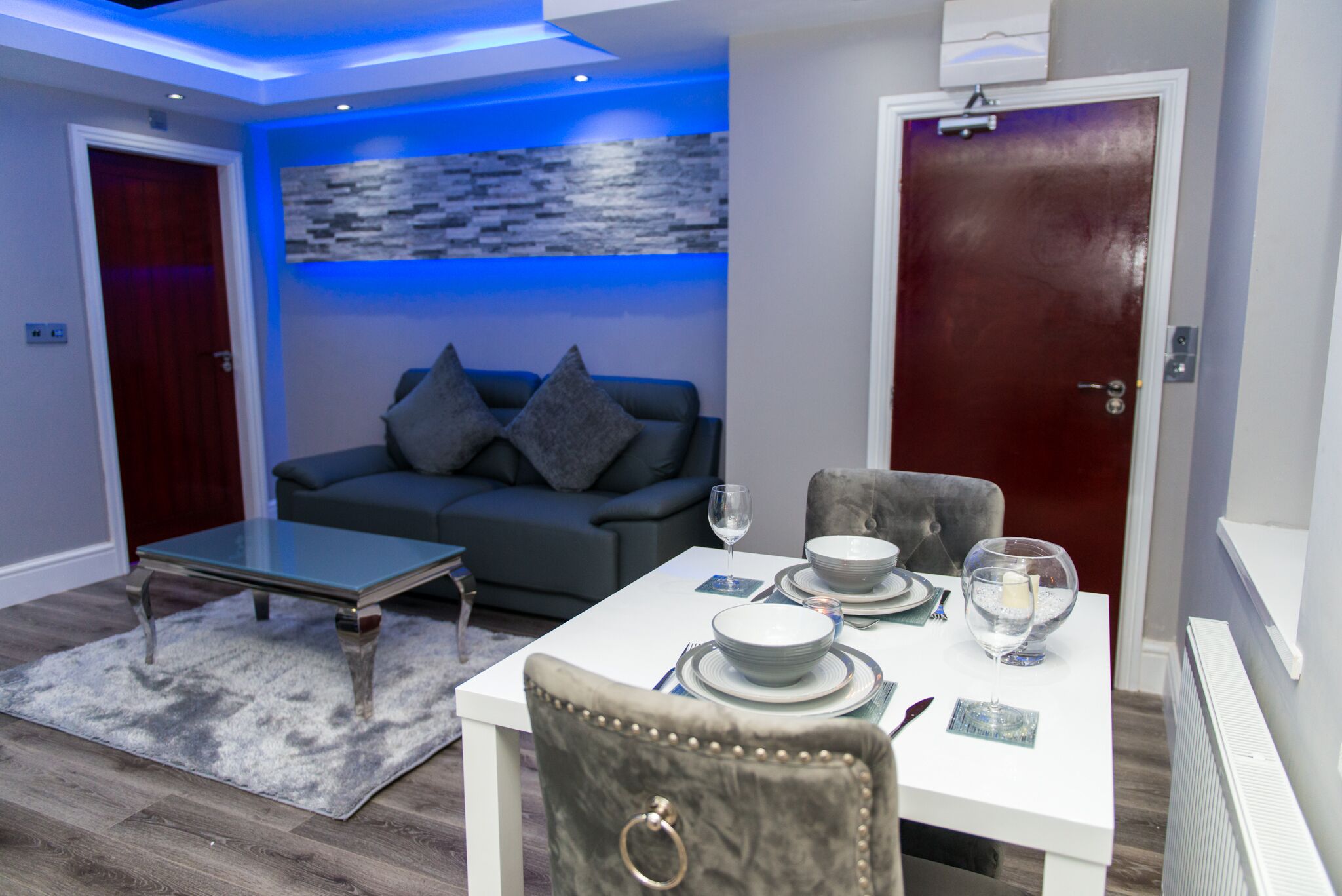 Ein modernes Wohnzimmer mit Essbereich, einem grauen Sofa, einem Glastisch und einer roten Tür.