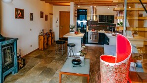 Un vaste espace de vie doté d’un haut plafond, de poutres apparentes, d’une cuisine et d’un escalier.
