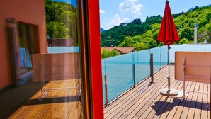Une terrasse en bois avec un parasol rouge, une balustrade en verre et une vue sur un paysage montagneux.