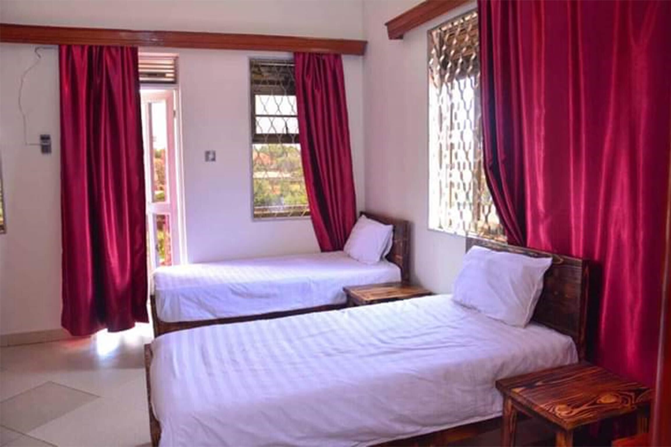 Een kamer met twee eenpersoonsbedden, houten hoofdborden en rode gordijnen.