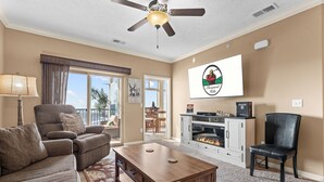 Ein Wohnzimmer mit Sofa, Sessel, Couchtisch, Kamin, Fernseher und Deckenventilator.