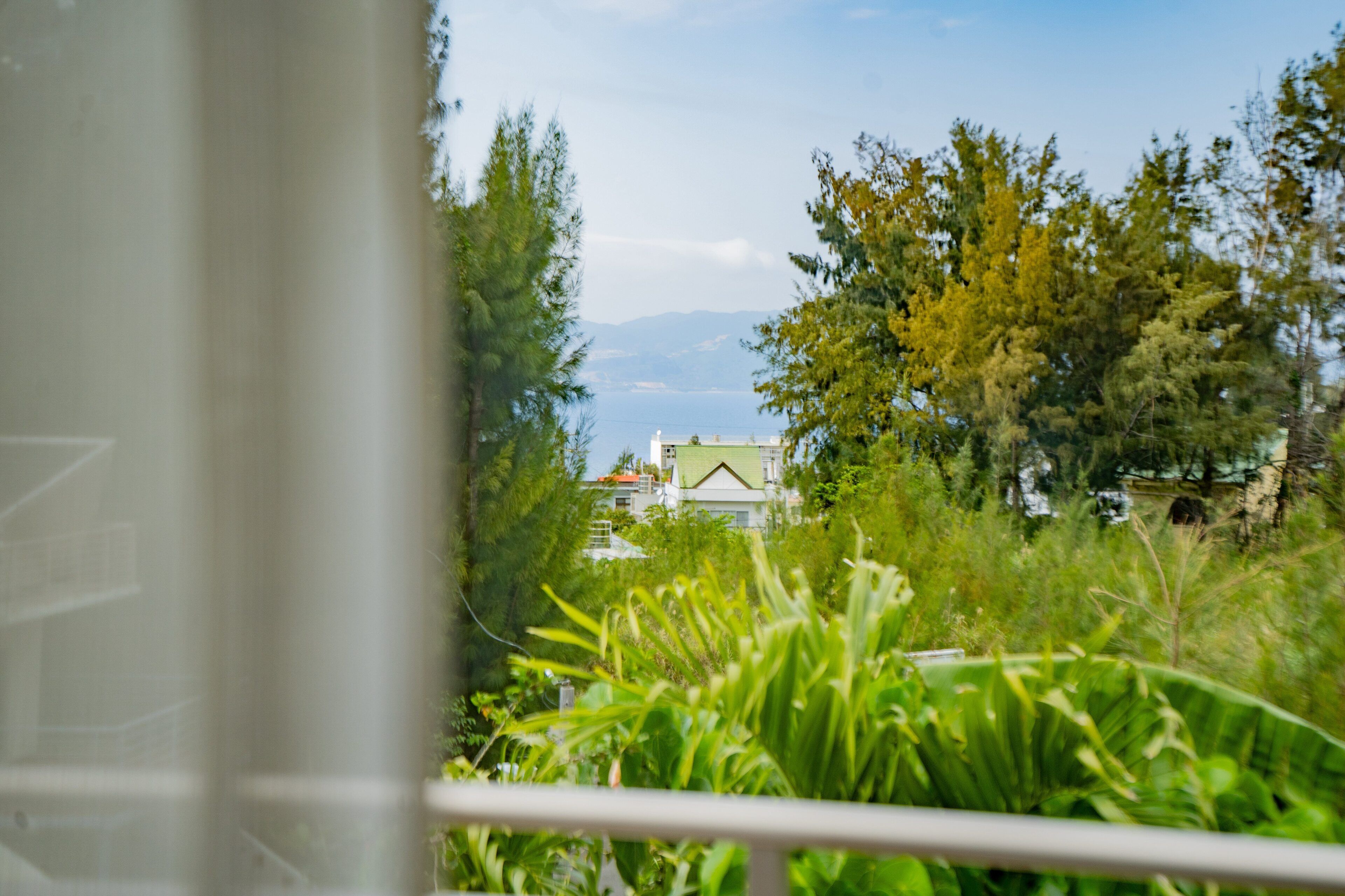 A view of a house surrounded by greenery, with a clear sky and mountains in the background.