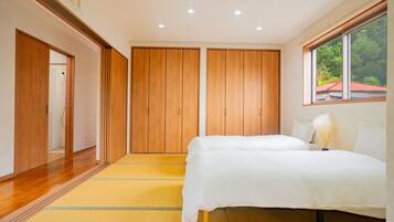 A bedroom with a bed, wooden wardrobe, and a window with a view of greenery.