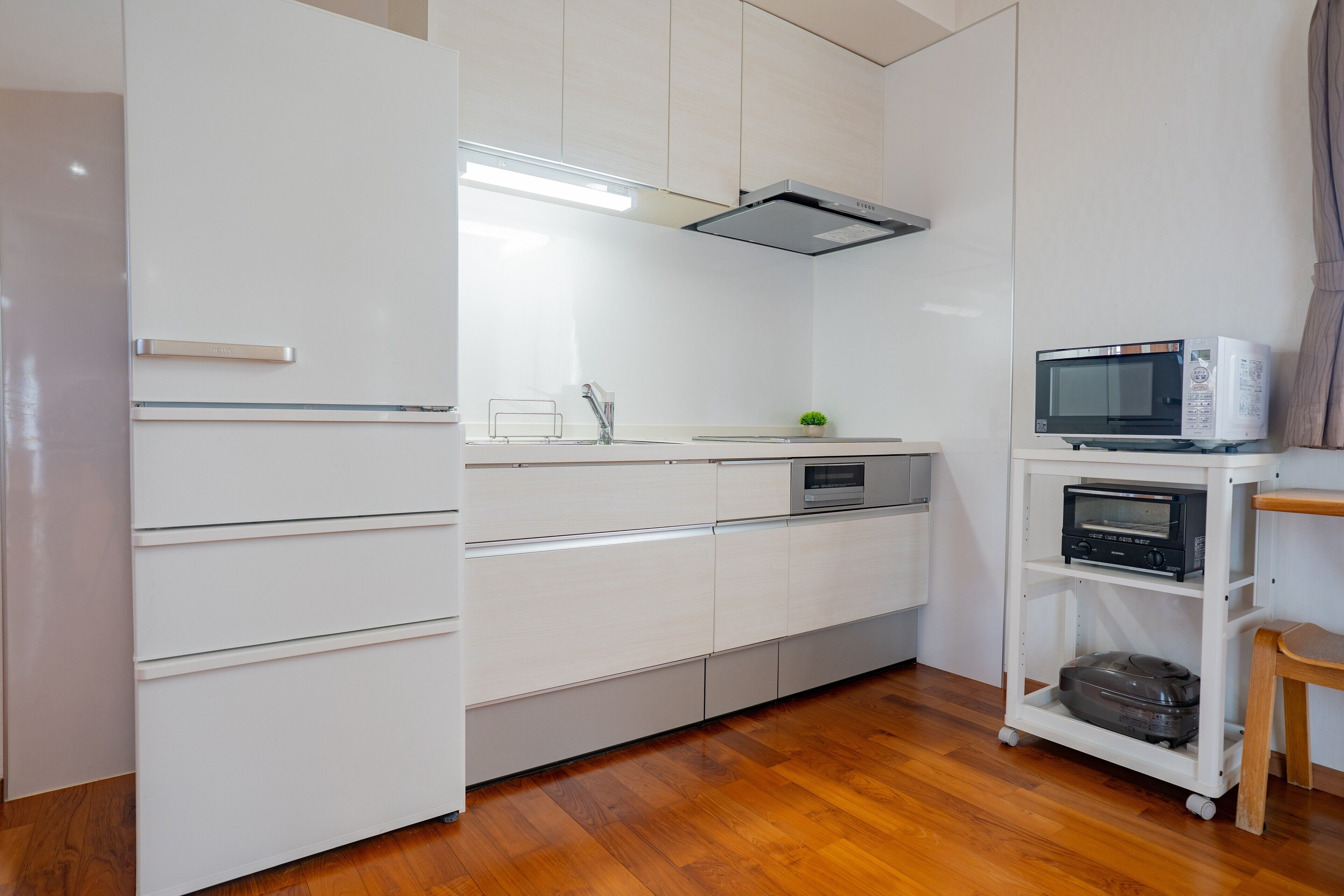 Una cocina compacta con muebles blancos, microondas, horno tostador y una pequeña estantería.