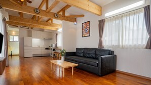 Un vaste espace de vie doté d’un plancher en bois, d’un canapé en cuir noir, d’une table basse en bois et d’une cuisine à l’arrière-plan.