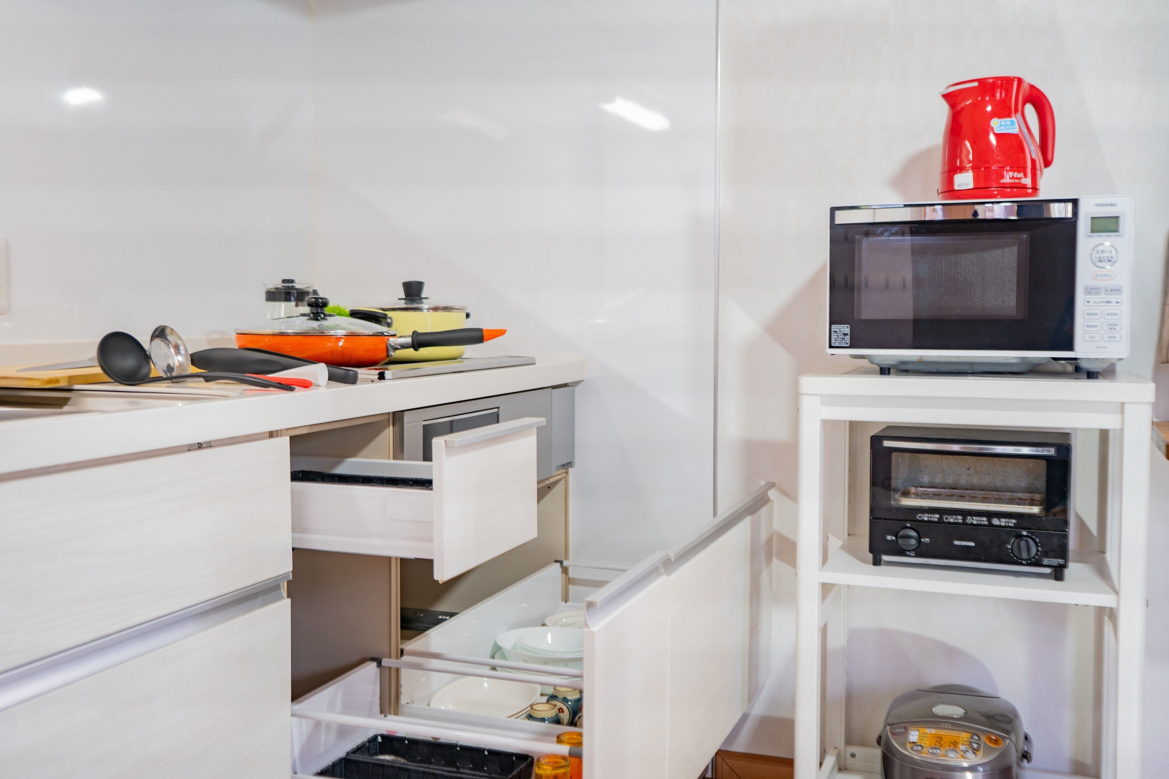 Cocina compacta con microondas, tostadora y cafetera sobre estantes, y un cajón con utensilios y vajilla.