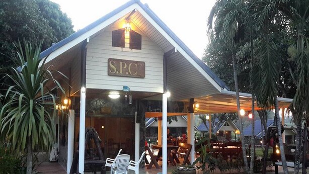 A building with a sign reading "S.P.C." and a covered outdoor seating area with chairs and tables.