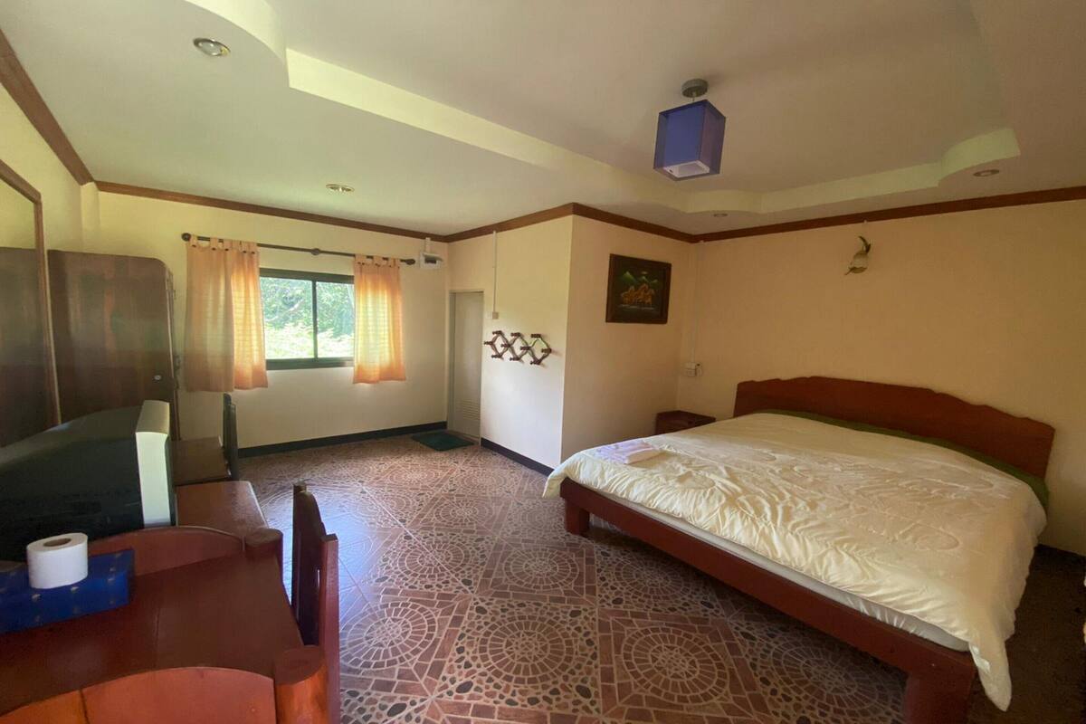 A hotel room with a bed, a desk with a chair, a TV, and a window with curtains.