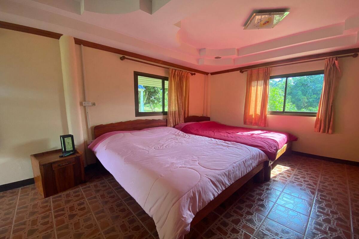 A bedroom with a large bed, two windows with curtains, a nightstand, and a ceiling light fixture.