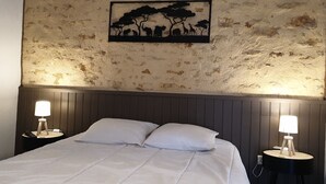 A bed with white bedding, two bedside lamps, a wooden headboard, and a wall with a textured surface and a framed picture of animals. - Small stone house in the heart of Périgord Noir (Salignac-Eyvigues)
