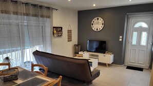 A living room with a sofa, TV, and a clock on the wall. - Small stone house in the heart of Périgord Noir (Salignac-Eyvigues)