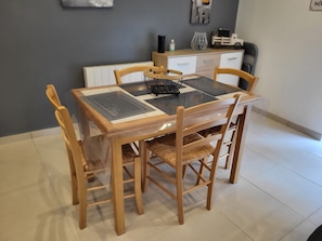 Un coin repas avec une table et des chaises en bois, un plateau en verre et un meuble blanc en arrière-plan.