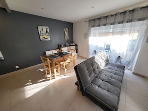Un salon avec un canapé, une table à manger et des chaises, et un tableau représentant un paysage urbain accroché au mur.