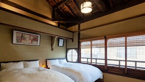 Habitación con dos camas, vigas de madera, una lámpara colgante y una ventana con persianas de bambú.