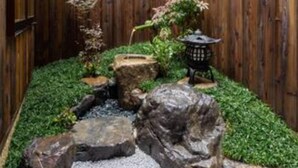 Una cerca de madera rodea un jardín con un pequeño estanque, rocas y un farol.