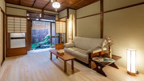 Una habitación tradicional japonesa con suelo de tatami, un sofá, una mesa de madera y un puertas correderas que dan a un jardín.