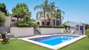 Un edificio moderno a due piani con piscina, area salotto esterna e verdeggiante giardino.