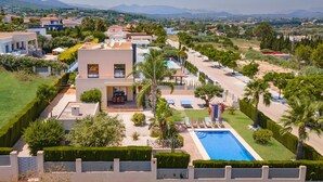 Una villa moderna con piscina, circondata da giardini curati e palme.