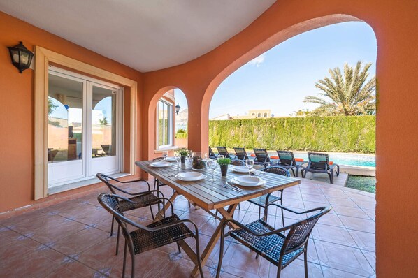 A patio with a table set for dining, surrounded by chairs, and overlooking a swimming pool.