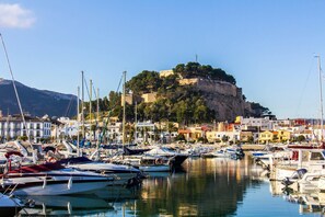 A marina with boats docked, a castle on a hill, and buildings in the background.