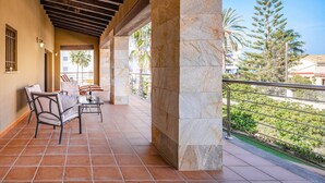 A covered outdoor area with tiled flooring, stone pillars, and a metal railing overlooking a landscaped garden. - 0646 Villa Amanda Beach (Denia)