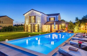 A two-story stone house with a swimming pool and outdoor seating area.