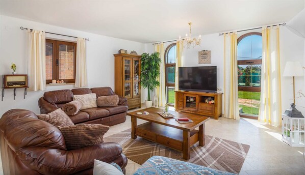 A living room with a leather sofa, a coffee table, a TV, and a large window with curtains.