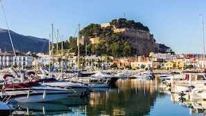 Un puerto deportivo con barcos amarrados, un castillo en una colina y edificios al fondo.
