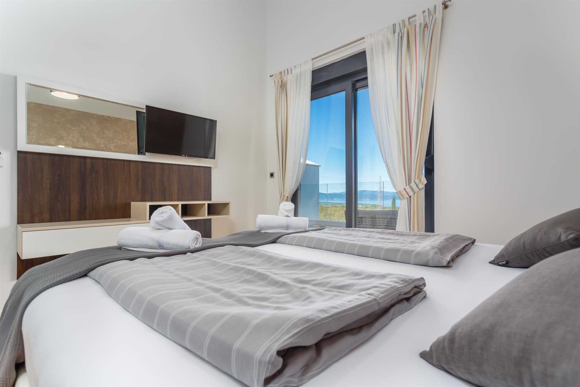 Ett hotellrum med två sängar, en tv som är monterad på väggen och ett stort fönster med gardiner.