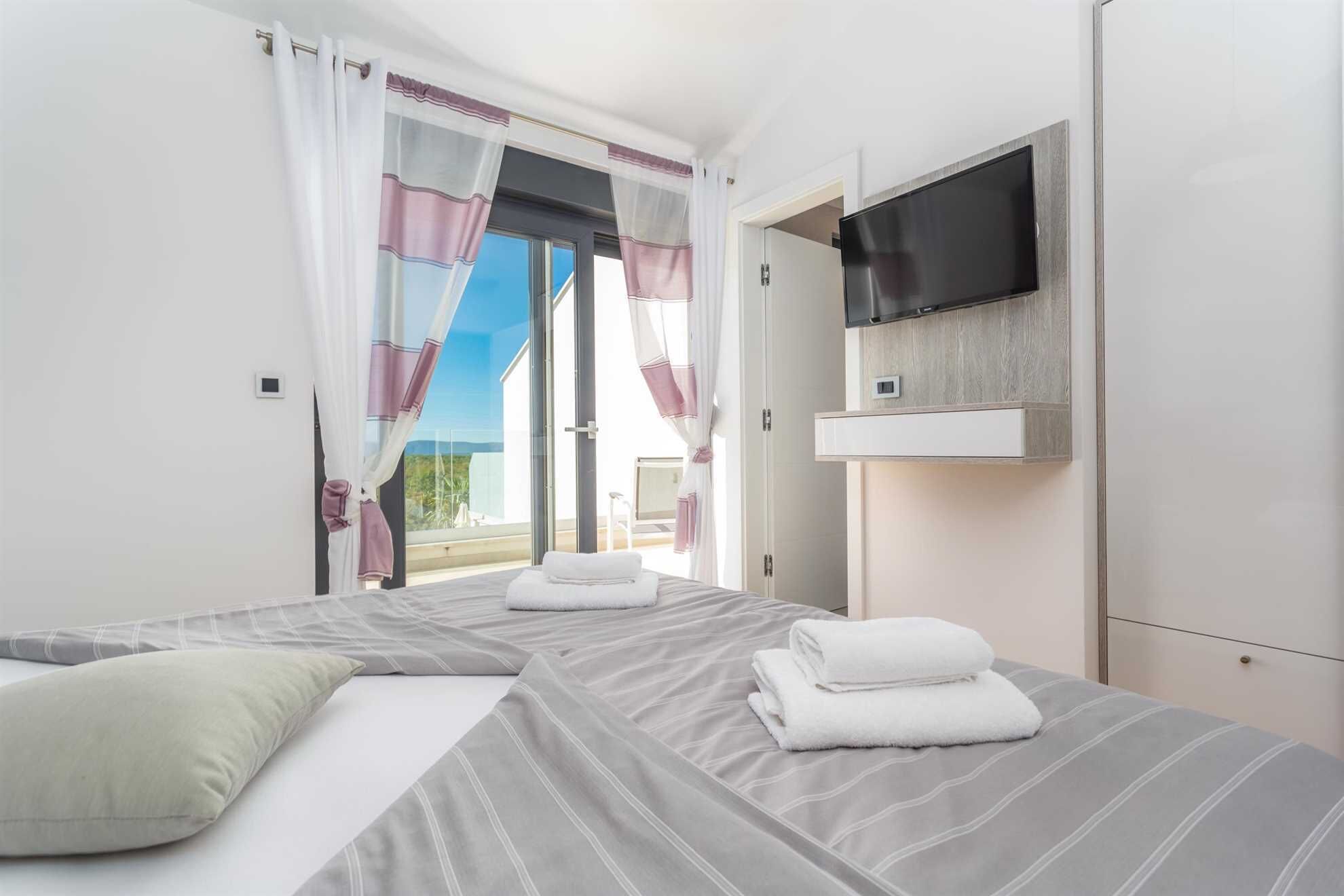 A hotel room with a bed, a TV mounted on the wall, and a view of the outdoors.