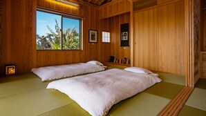A traditional Japanese-style room with tatami flooring, two beds, a large window with a view of palm trees, and wooden walls. - Yamagata Ryukyu Hatago Onna Bokairo (Onna)