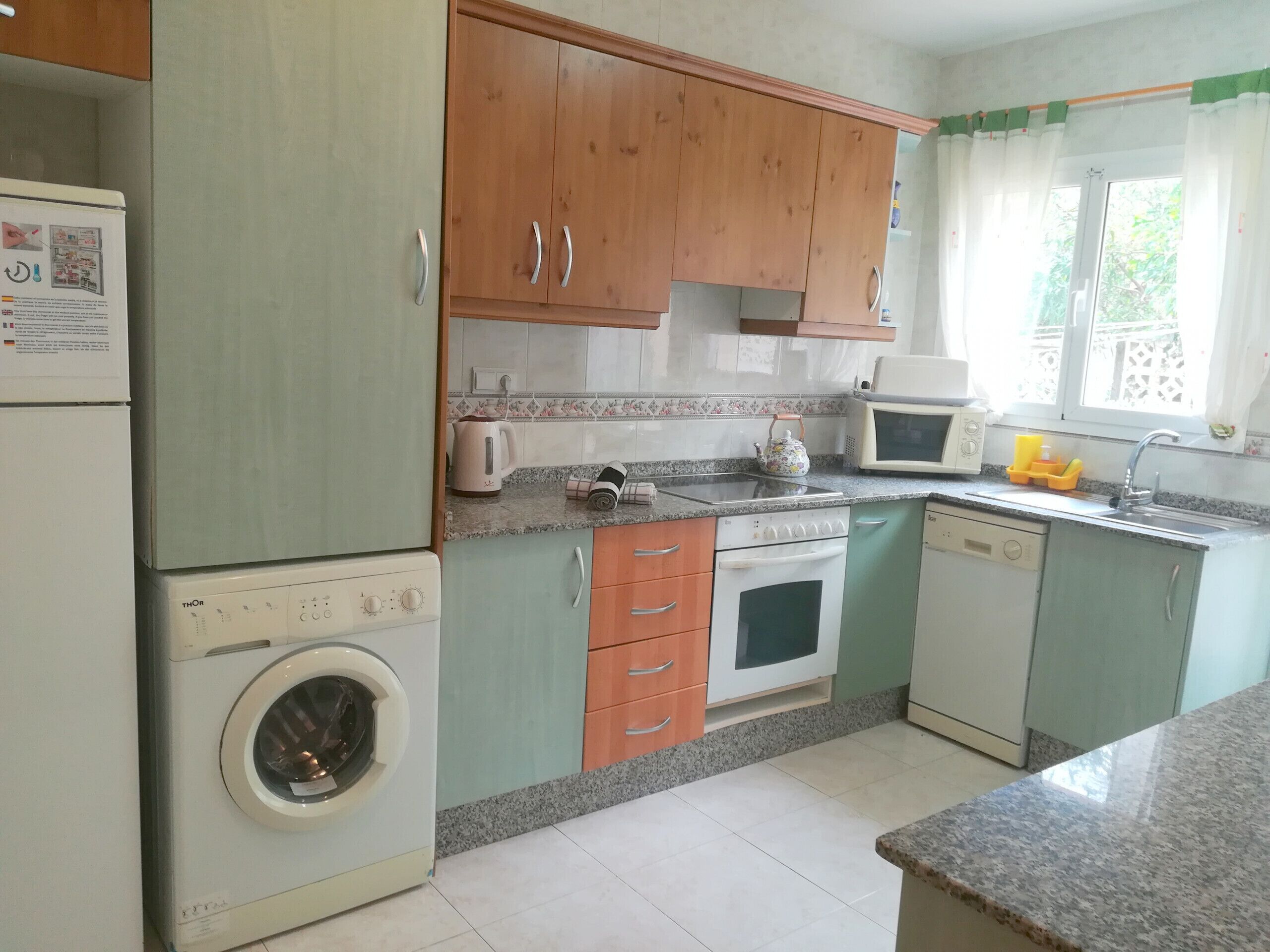 A compact kitchen with wooden cabinets, a washing machine, an oven, and a microwave.
