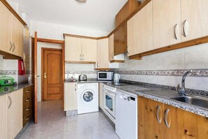 Una cocina compacta con armarios de madera, lavadora, microondas y fregadero.