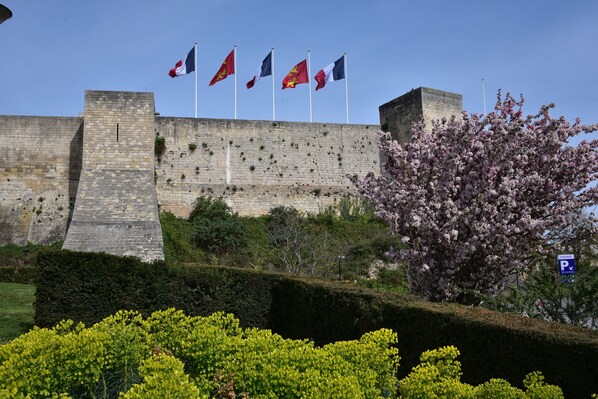 A historic stone wall with flags, a flowering tree, and a parking sign. - Bright, spacious apartment in the city center (Caen)