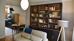 A living room with a sofa, a wooden bookshelf, and a dining area with a table and chairs.