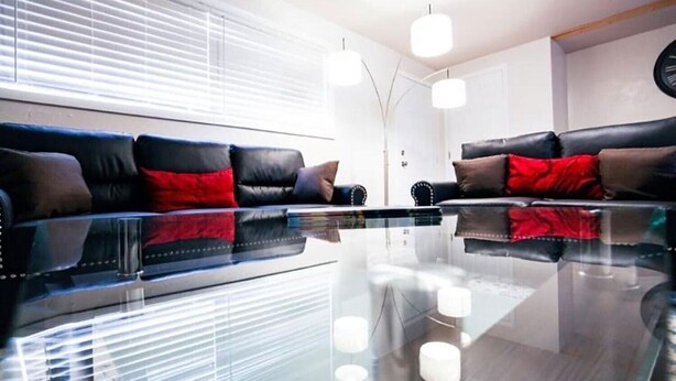 Ein modernes Wohnzimmer mit einem Glastisch, Ledersofas mit roten Kissen und Pendelleuchten.