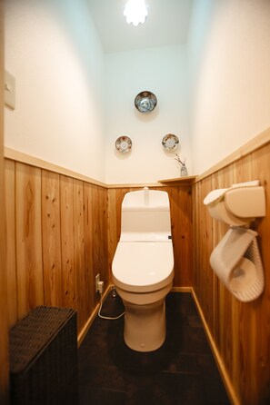A small, wooden-paneled bathroom with a white toilet, a bidet, and a wall-mounted toilet paper holder.