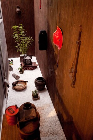 A narrow corridor with a wooden door, a red lantern, and a small potted plant.