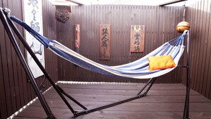 A hammock chair with an orange pillow, set against a wooden wall with vertical slats and hanging decorations. - Yamagata Kyomachi Hatago Kitayamaomiya (Kyoto)