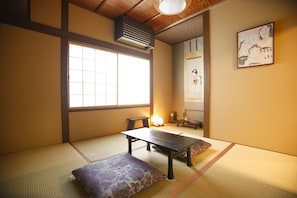 Una habitación tradicional japonesa con suelo de tatami, una mesa baja, un cojín y una puerta corredera.