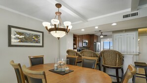 Un coin repas avec une table ronde en bois, six chaises, un lustre et une œuvre d’art encadrée accrochée au mur.
