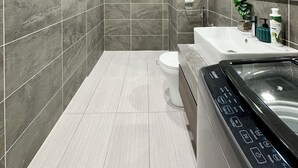 A modern bathroom with grey tiles, a white toilet, a bathtub with a control panel, and a shower area.