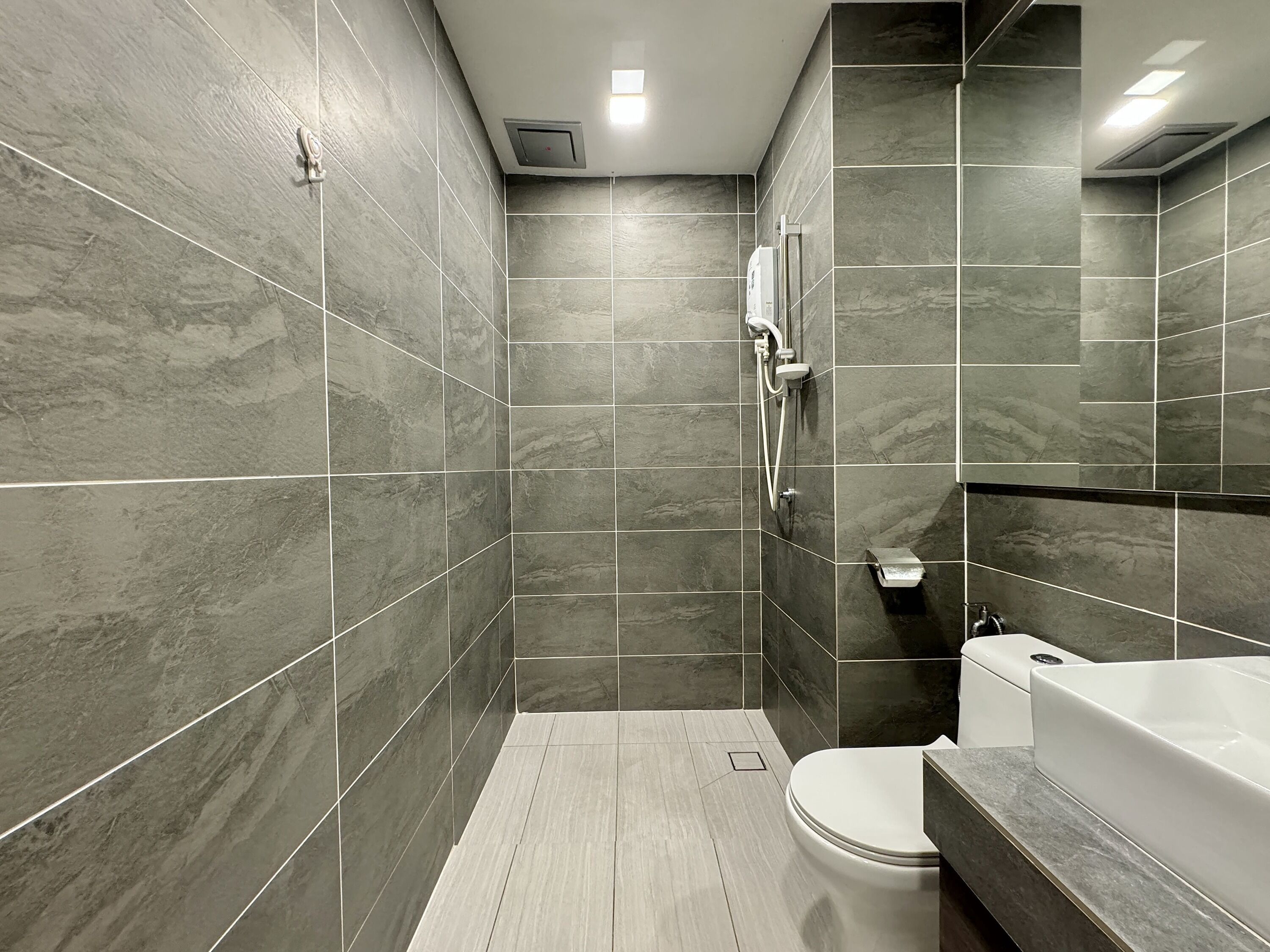 A modern bathroom with grey marble tiles, a white toilet, a bathtub, and a shower area.