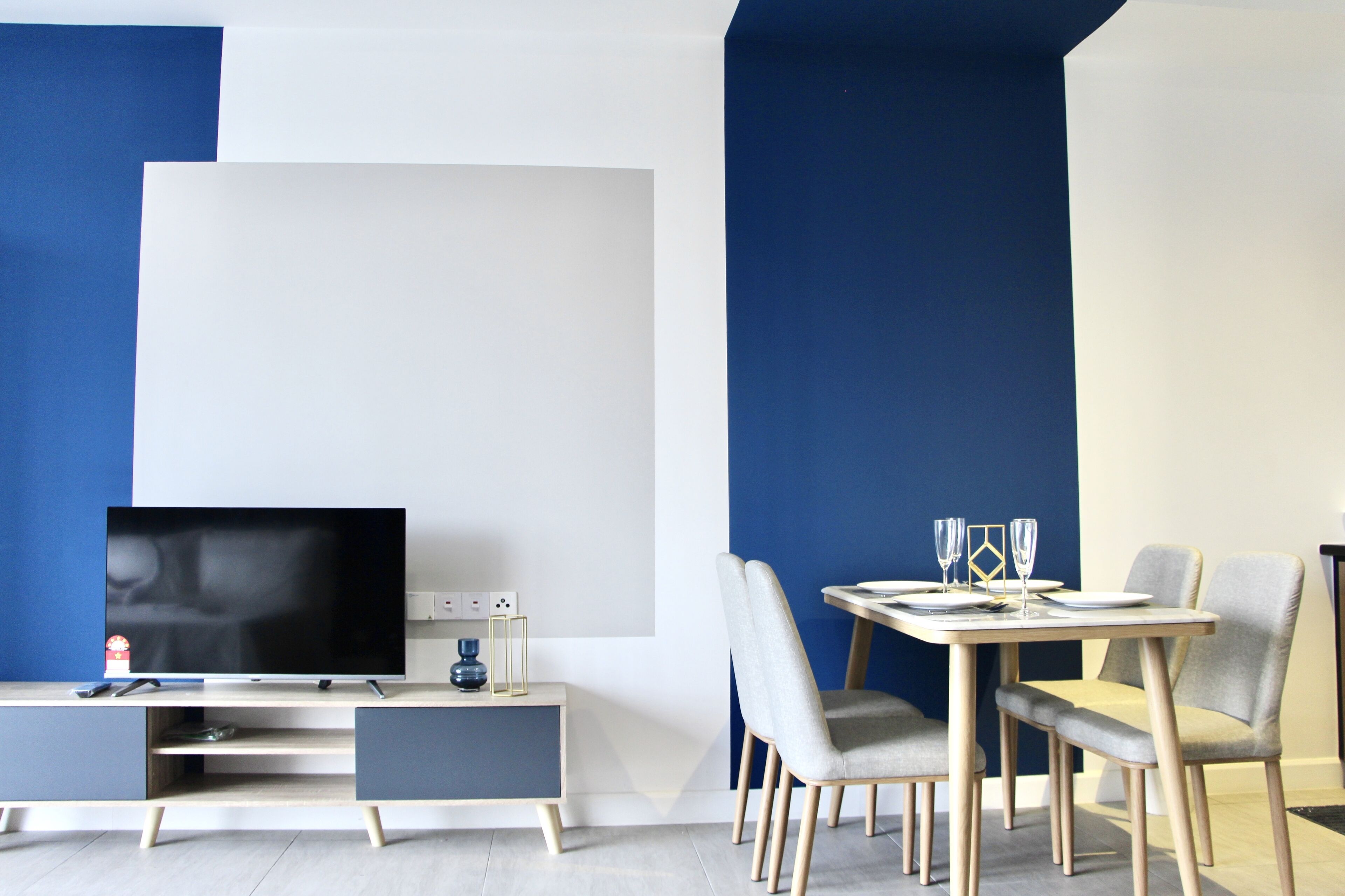 A modern living room with a flat-screen TV, a small table with two chairs, and a dining table set for two.
