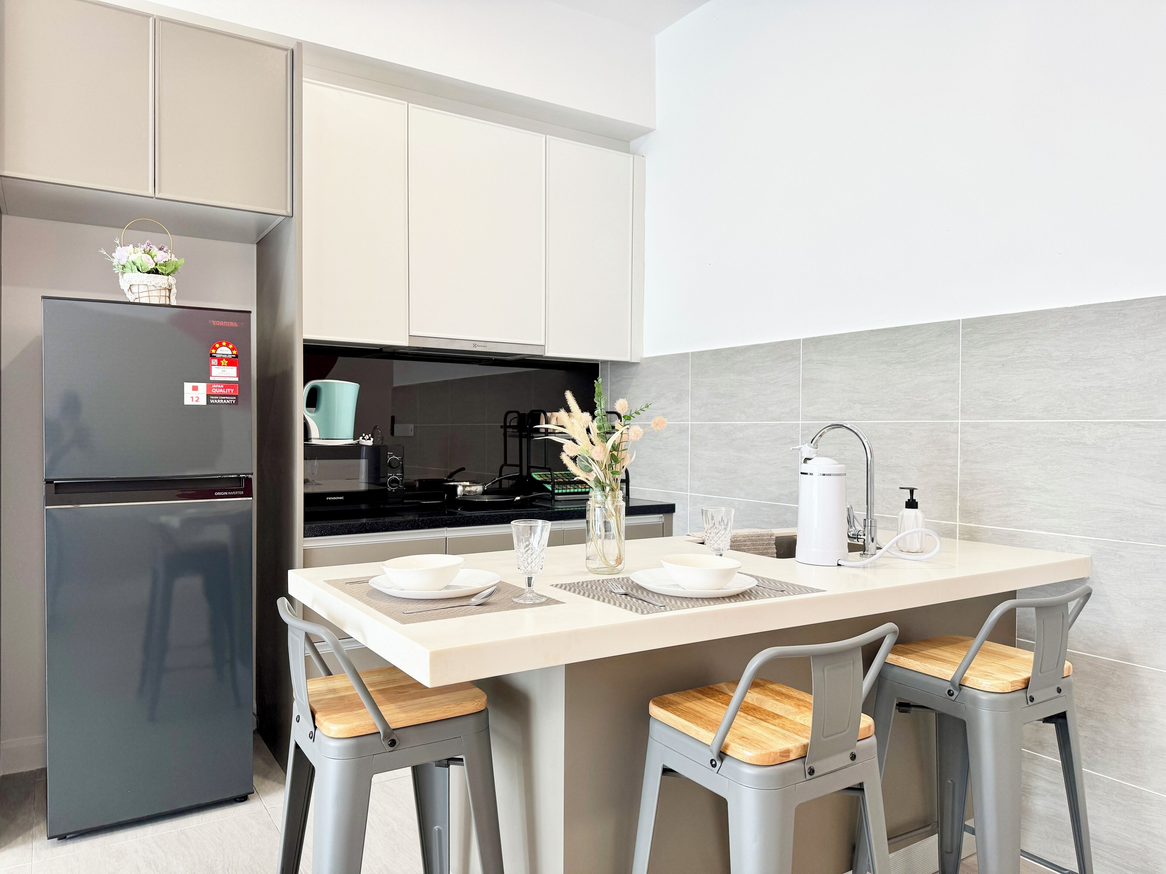 Una cocina moderna con refrigerador empotrado, estufa y pileta. Hay dos taburetes de bar con asiento de madera y una mesita con un florero.