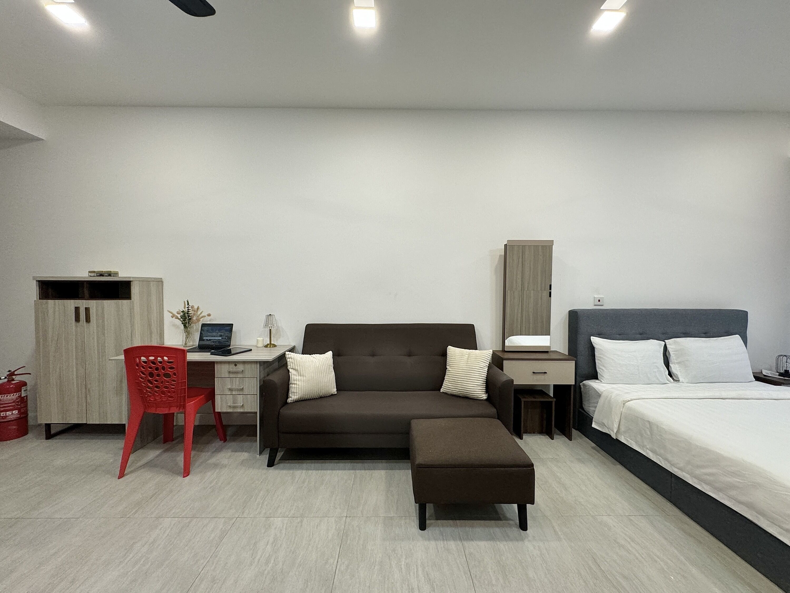 A modern hotel room with a sofa, a desk, a bed, and a wardrobe.